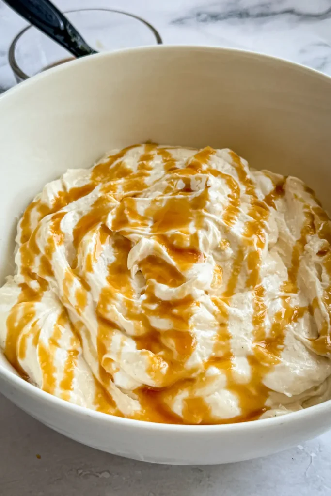 The salted caramel cheesecake dip in a large white bowl after being drizzled with caramel.
