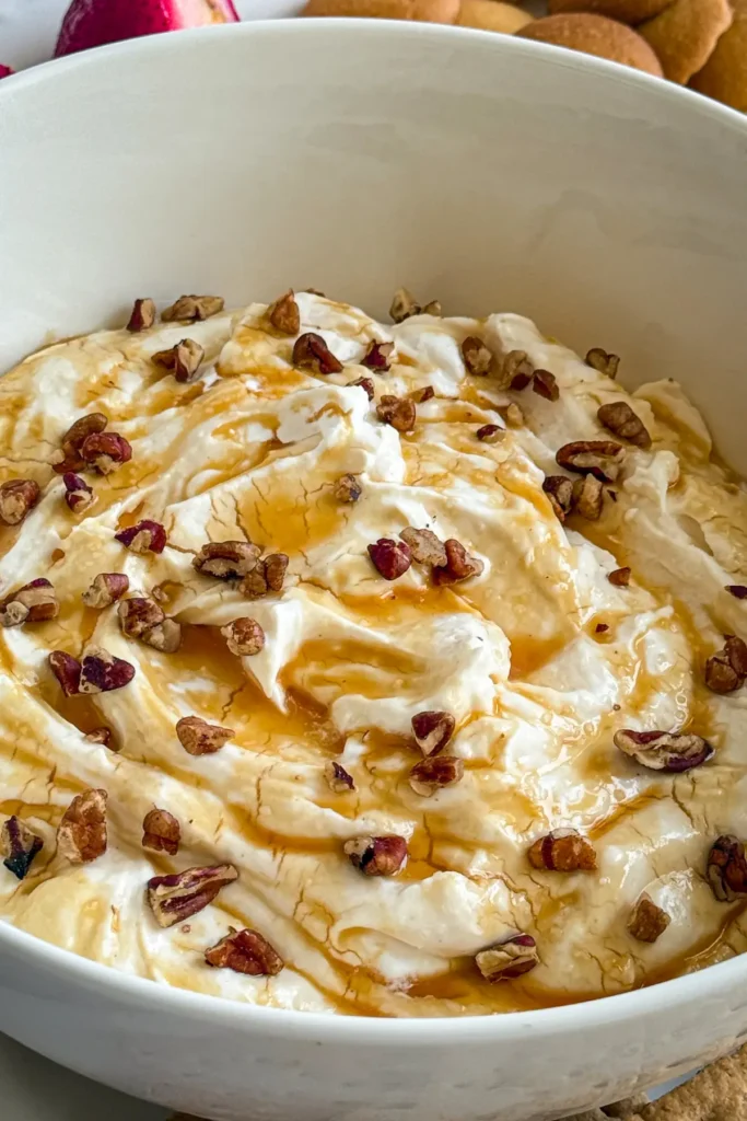 A close-up of a big bowl of salted carame cheesecake dip topped with chopped pecans.