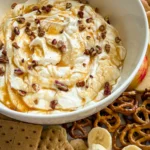 A large bowl of Greek yogurt salted cheesecake dip topped with chopped pecans surrounded by graham crackers, pretzels, banana slices, and strawberries.