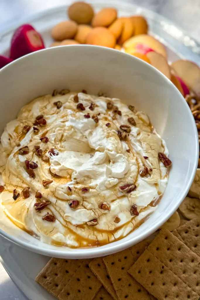 The salted caramel cheesecake dip surrounded by dippers on a white platter on a counter.