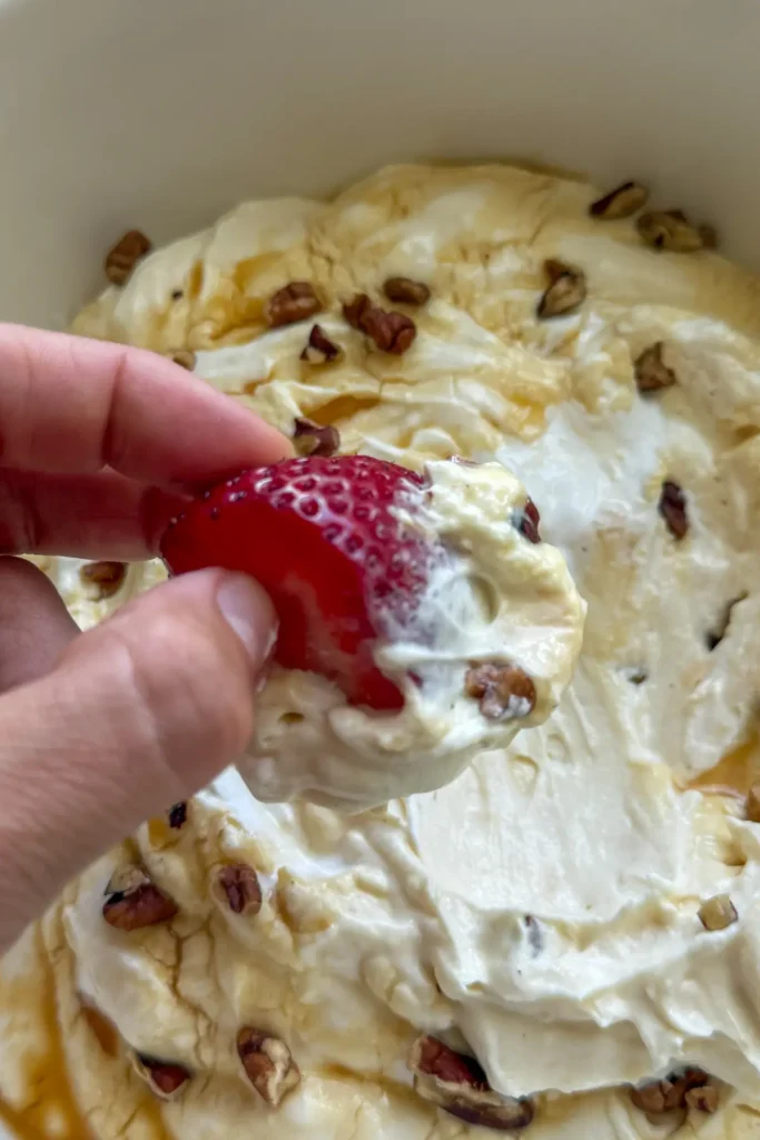 A strawberry being dipped in a large white bowl of cheesecake dip.
