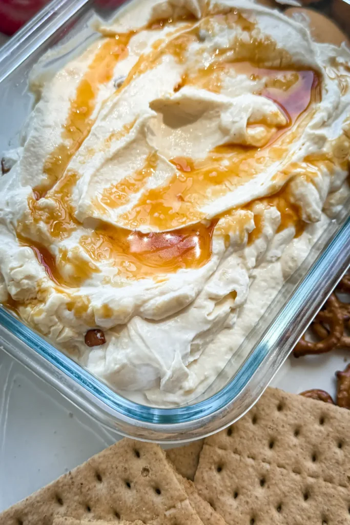 A close-up of easy salted caramel cheesecake dip in a meal prep storage container topped with caramel sauce.