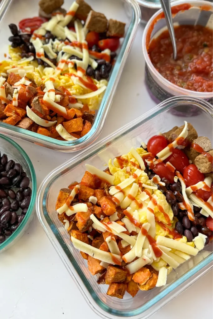Two glass meal prep containers with fully assembled sweet potato breakfast bowls next to a bowl of salsa.