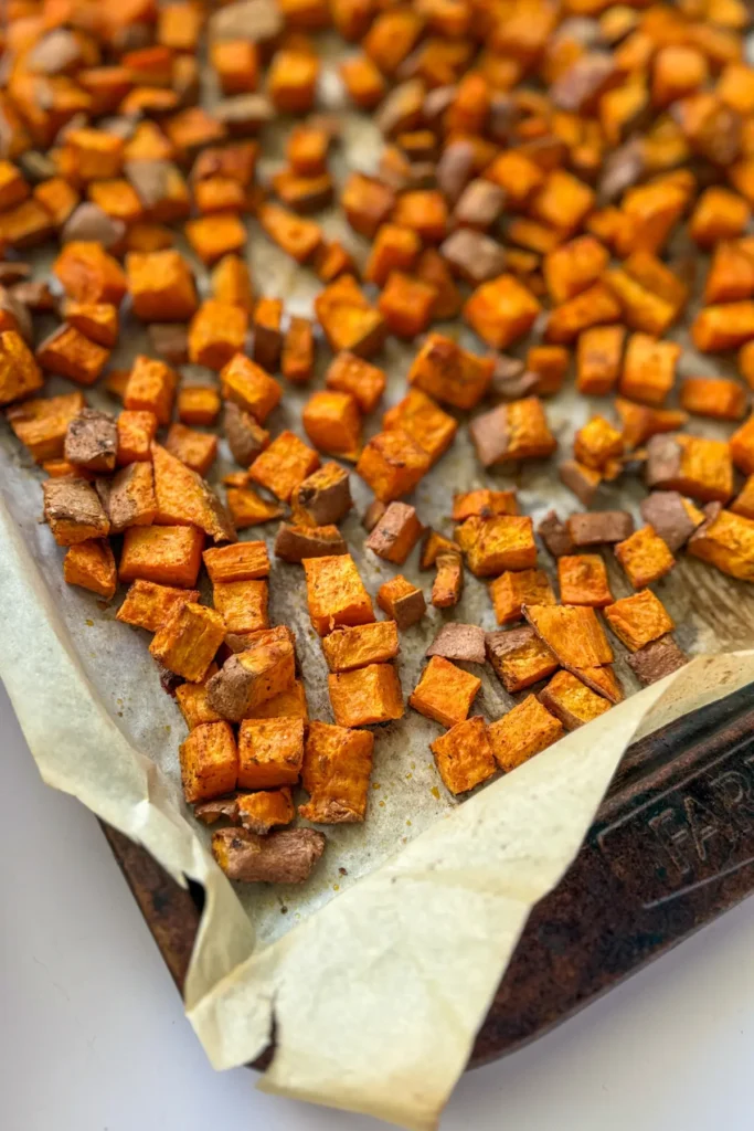 A baking sheet lined with parchment paper with roasted sweet potatoes on it.