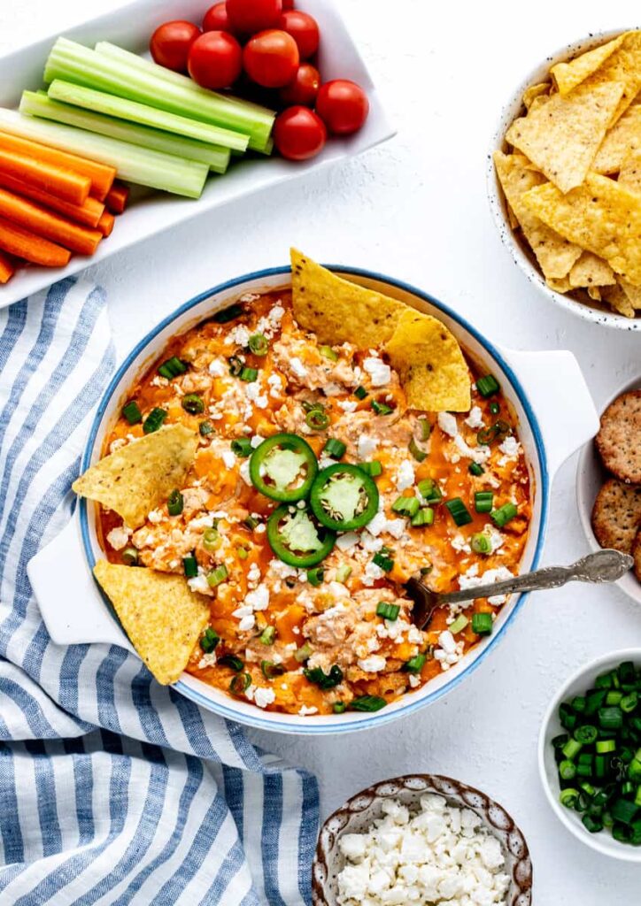 A birds-eye view of buffalo chicken dip in a bowl on a table next to celery and carrots.