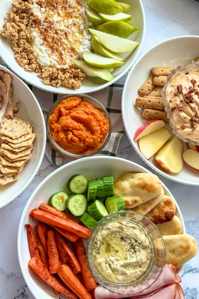 Four fall-inspired snack plates on a counter with a glass bowl of pumpkin puree in the middle.