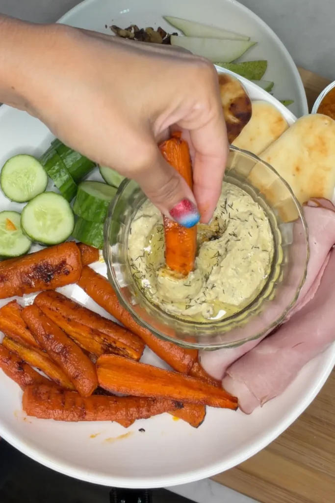 Someone dipping a carrot into the hummus on a snack plate.