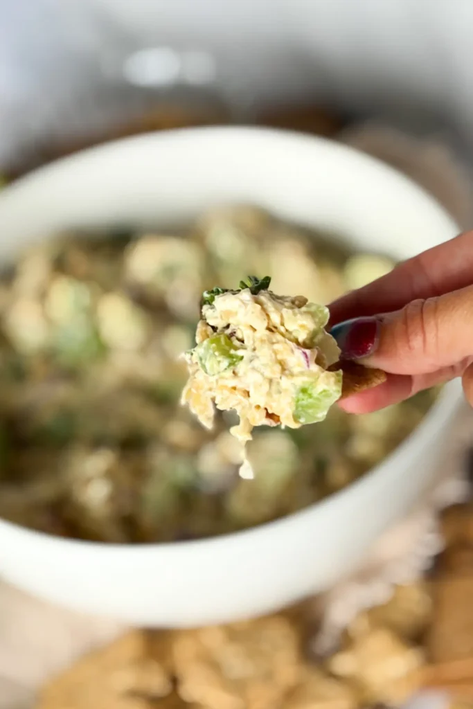 A Wheat Thin with honey mustard and apple chicken salad on it and a big bowl in the background.