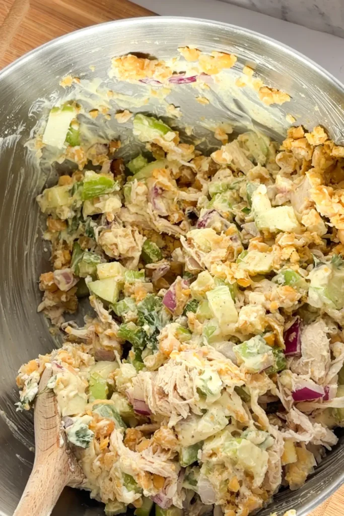 A spoon mixing the dressing into the chicken salad.