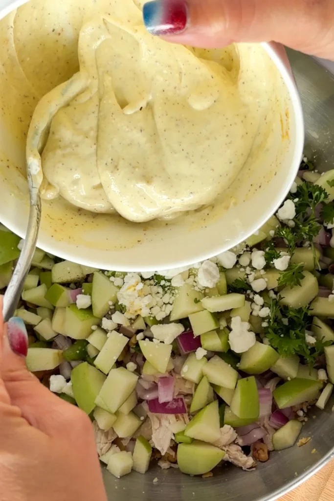 Adding the honey mustard sauce to a large bowl of ingredients for the chicken salad.