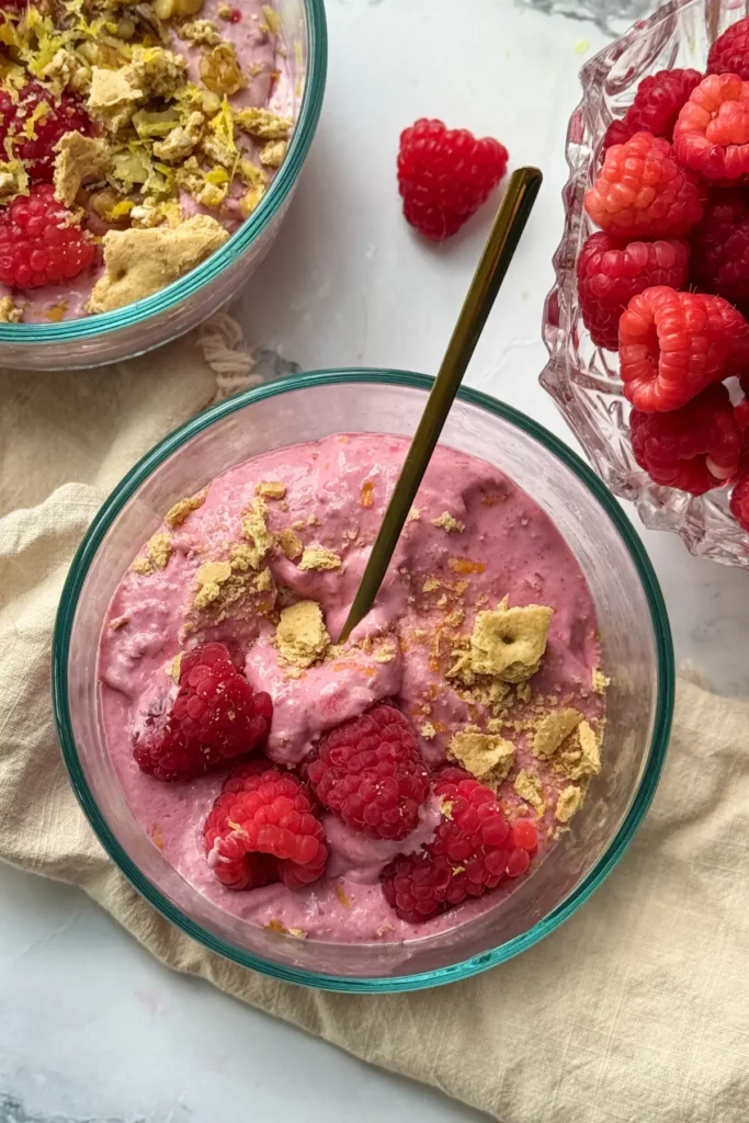 A spoon digging into a bowl of high protein frozen fruit whip on a counter next to a towel and another bowl.