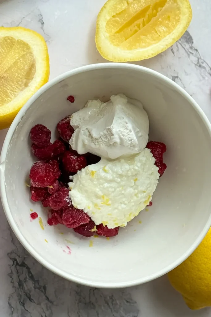 The ingredients for the protein whip in a large white bowl next to lemon wedges.