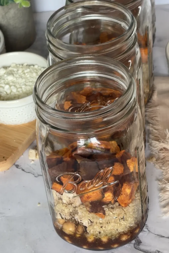 Adding the sweet potatoes into the salad jars on a counter.