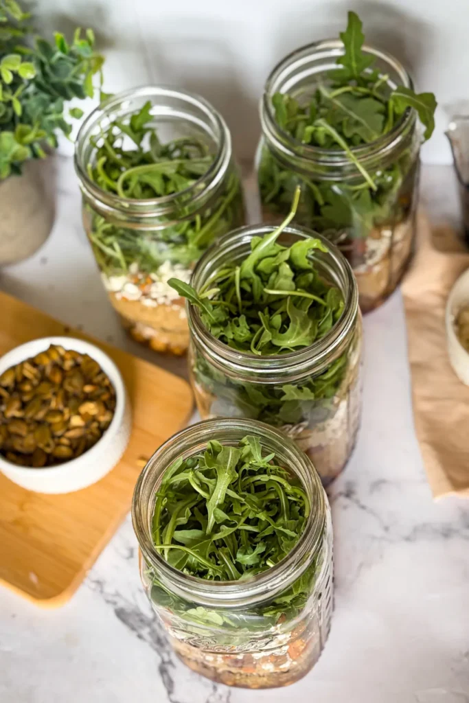 A birds-eye view of the fully assembled four meal prep salad jars without lids on them on a counter next to a bowl of pepitas.