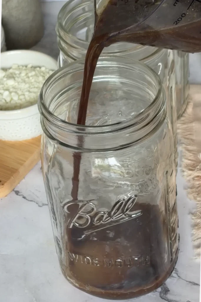 Pouring the maple balsamic dressing into the first salad jar.