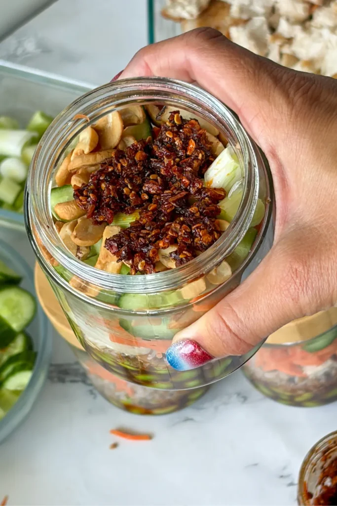 A close-up of a jar with chili crunch on top in someone's hand.