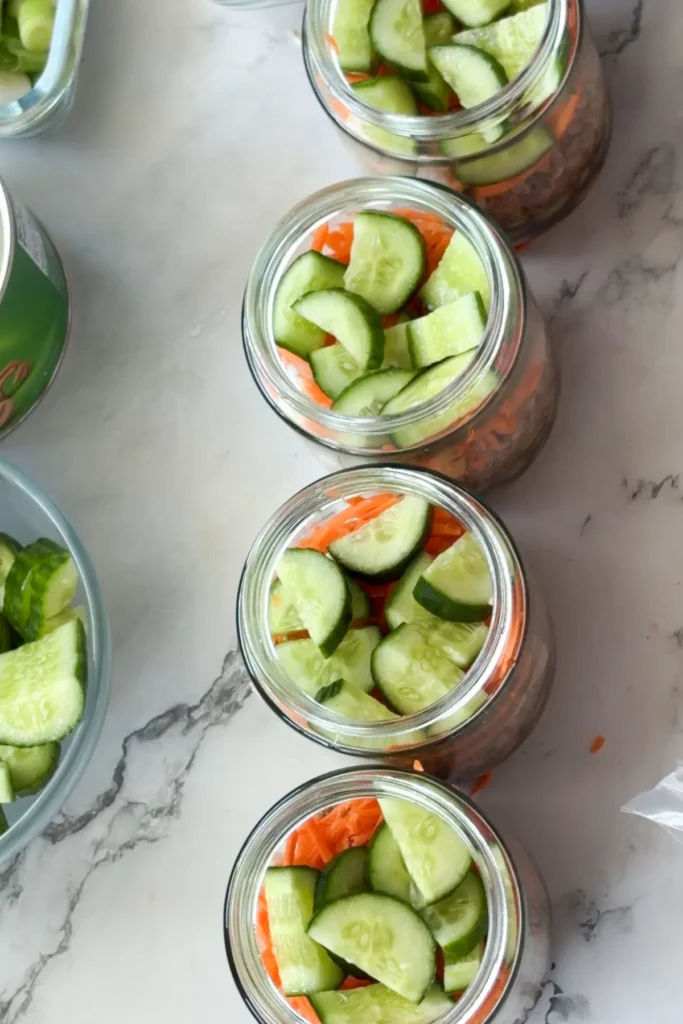 Half assembled meal prep salad jars on a counter next to the components.