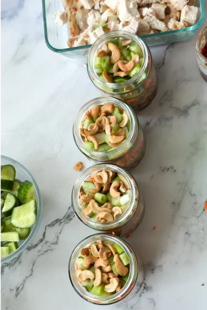 Four meal prep salad jars topped with cashews on a counter.