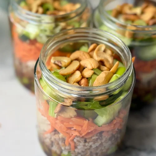 Three meal prep salad jars fully assembled in opened jars on a counter.