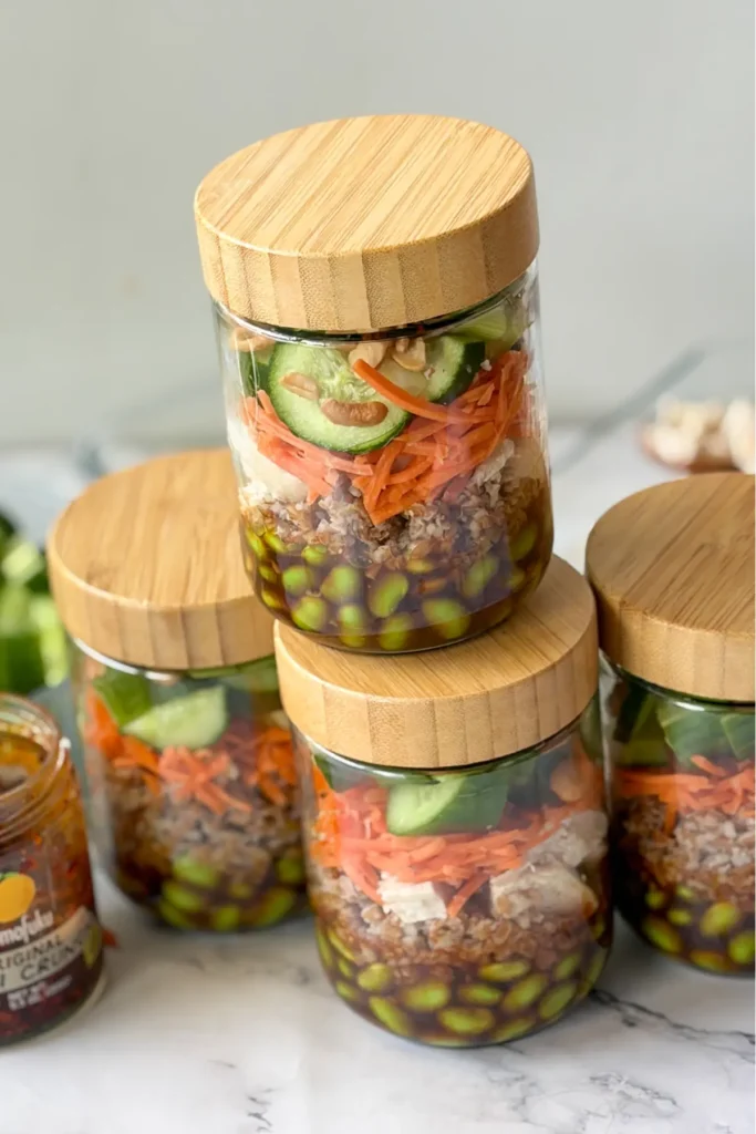 Four fully assembled meal prep salad jars with the lids on them lined up on a counter.