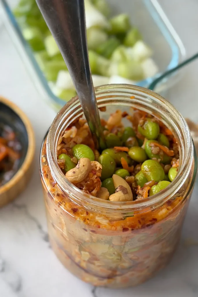 A salad jar after it has been shaken with a spoon in it on a counter next to the jar lid.