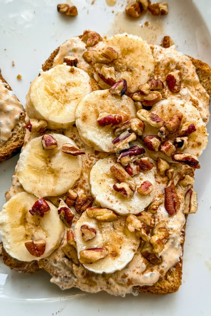 A birds-eye view of a piece of toast with cottage cheese pumpkin crewam cheese, banana slices, and chopped walnuts on a plate.