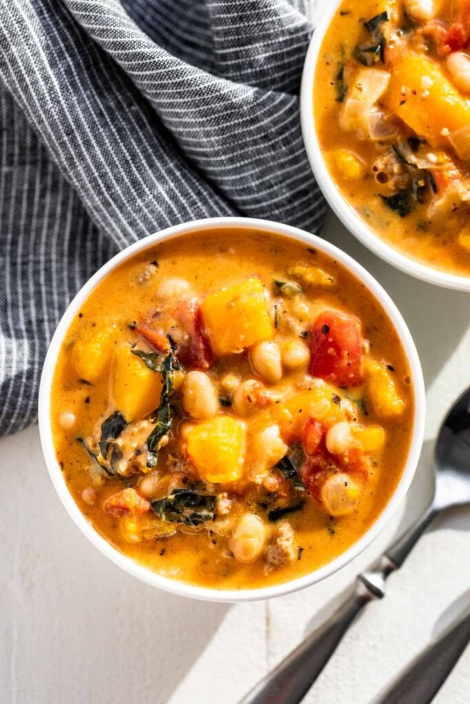 Two bowls of hearty butternut squash and sausage soup on a counter next to towels.