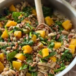 A large skillet with cooked ground turkey, butternut squash, spinach, and beans in it with a wooden spoon on a counter.