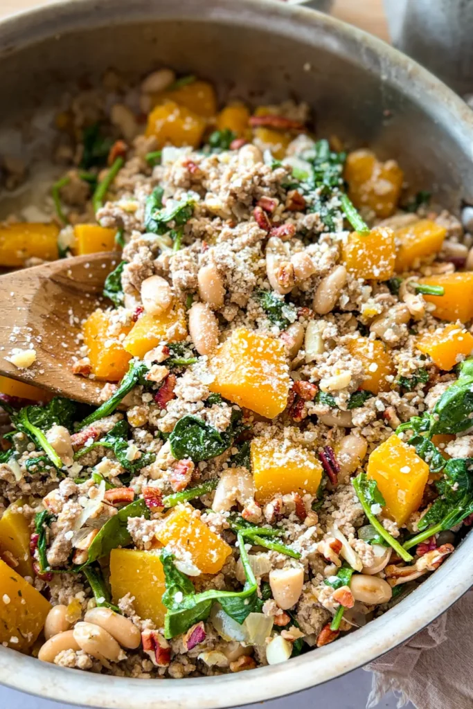 A birds-eye view of a fully cooked skillet topped with pecans and parmesan cheese with a wooden spoon in the pan.