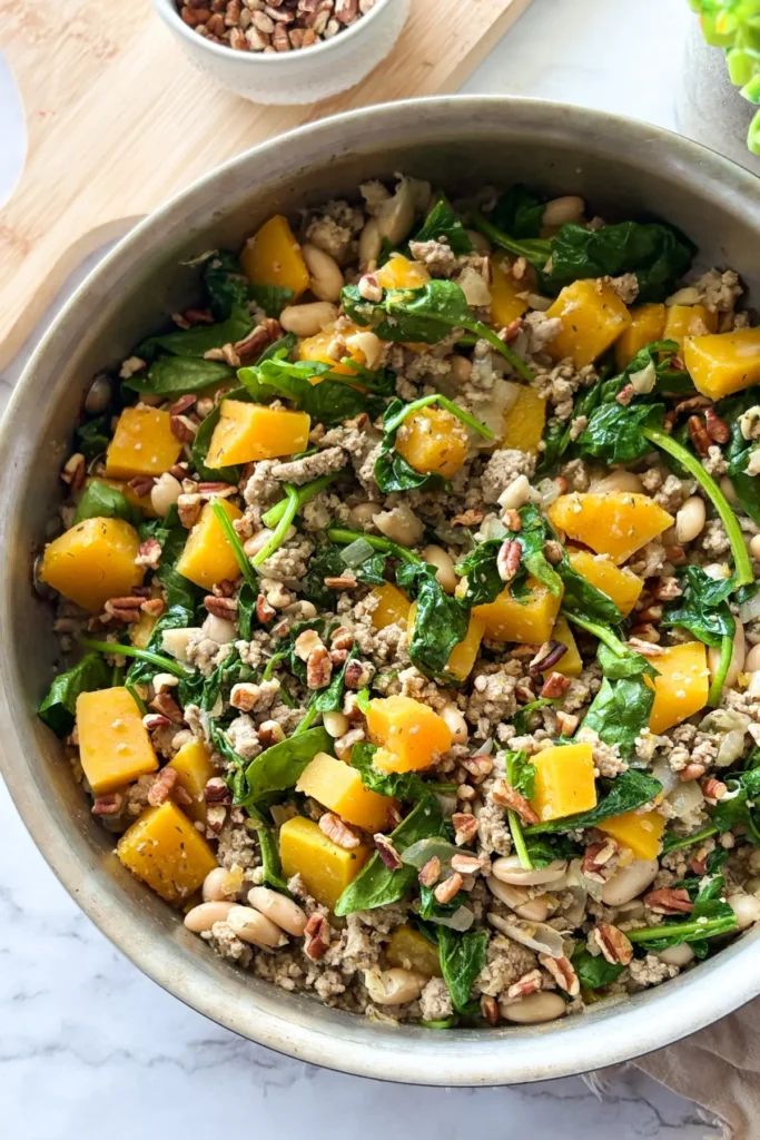 A birds-eye view of the one pan meal in a stainless steel pan on a counter next to a bowl of pecans.