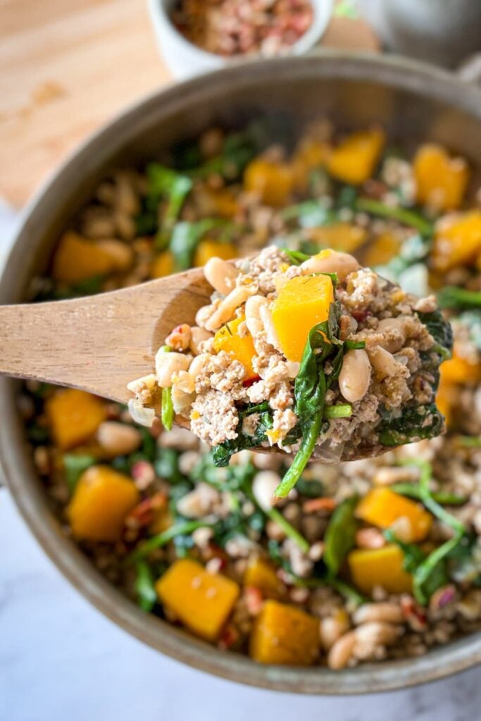 A large wooden spoonful of the turkey and butternut squash skillet over a large pan on a table.
