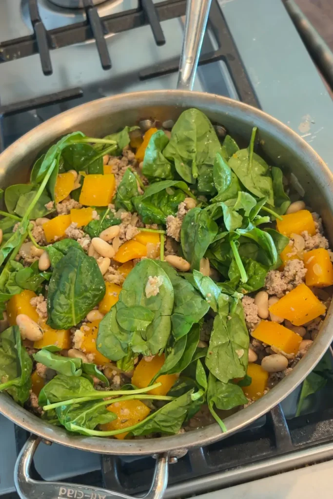 Adding the spinach and ground turkey into the skillet with the butternut squash in it.