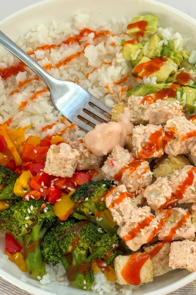 A crispy tofu bowl with veggies served over rice and drizzled with bang bang sauce and sriracha.