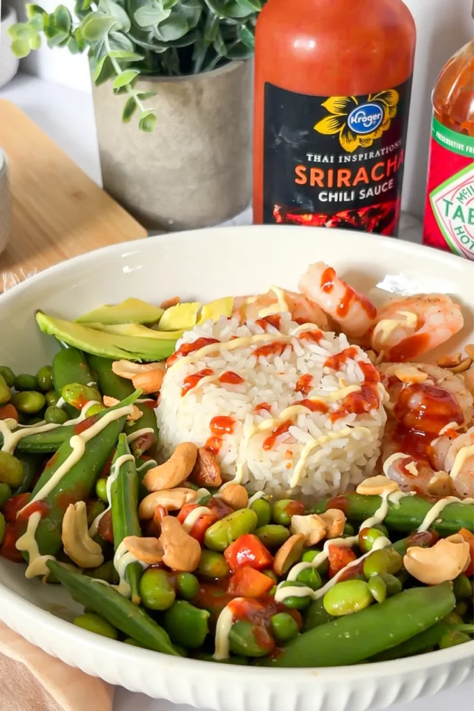 A shrimp and rice edamame bowl drizzling with sriracha on a counter.