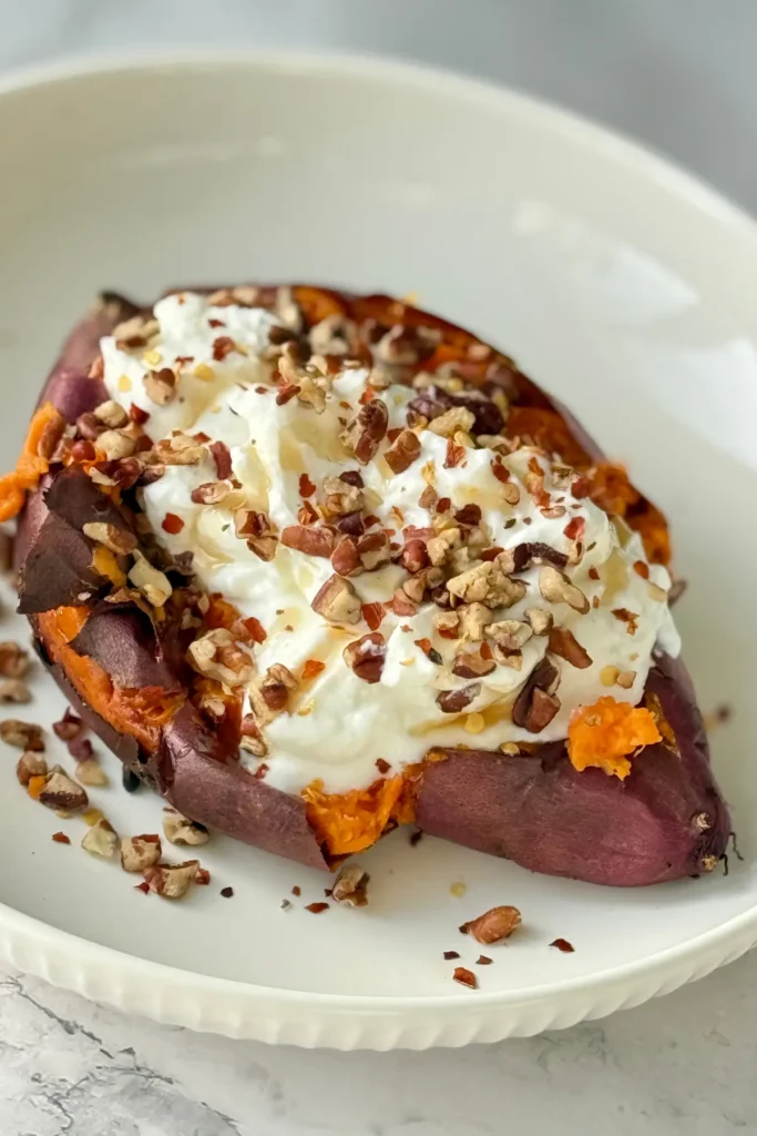 A roasted sweet potato topped with Greek yogurt and chopped pecans on a plate.