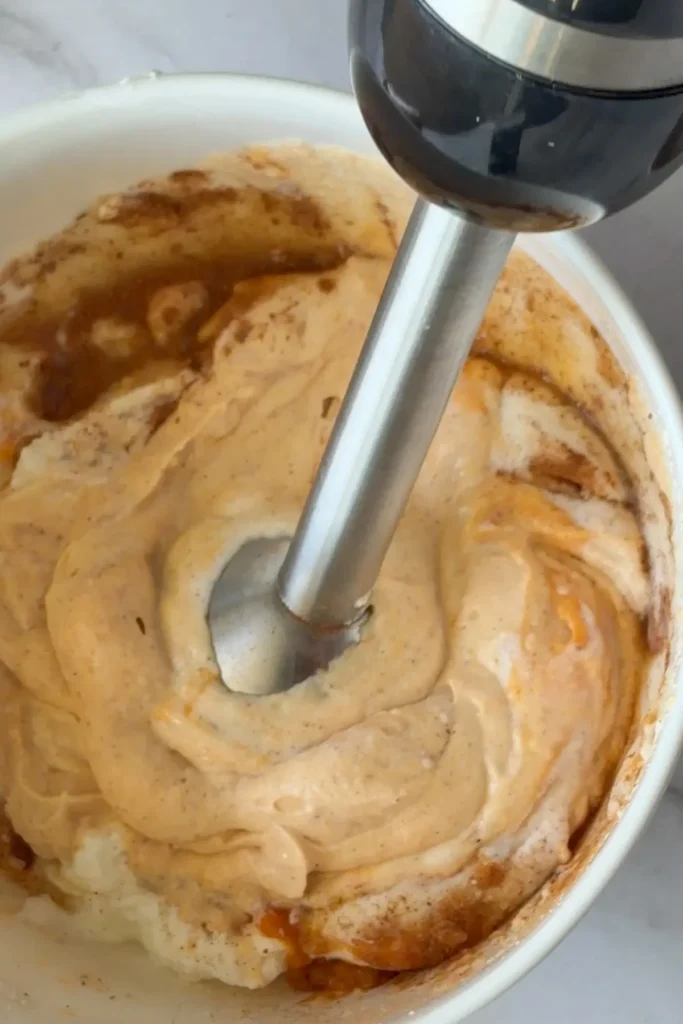 An immersion blender blending the ingredients in a bowl.