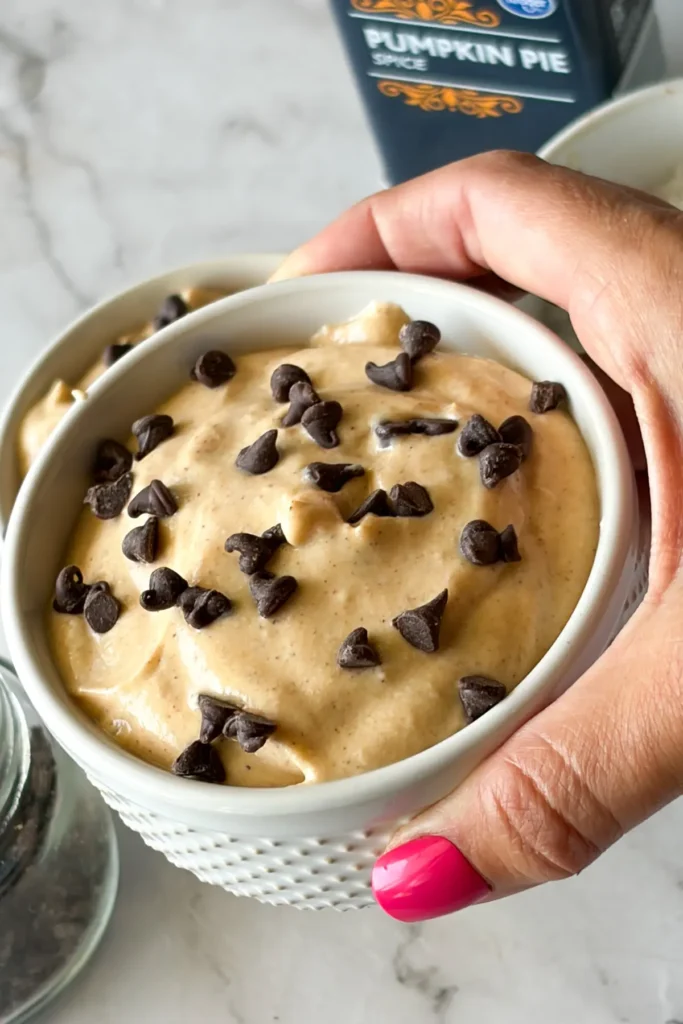 Someone holding up a small white ramekin with pumpkin cannoli dip in it with mini chocolate chips on top.