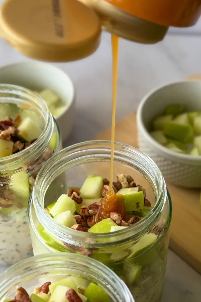 Caramel being drizzles onto the apples in an overnight oats jar.