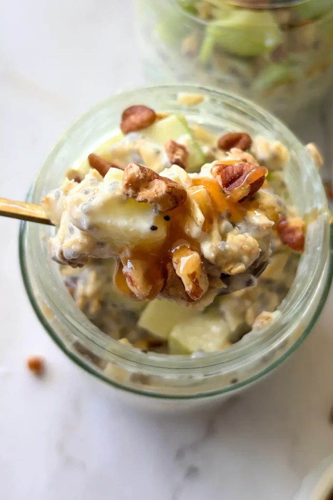 A close-up of a spoonful of the salted caramel apple overnight oats over a jar of fully assembled oats.