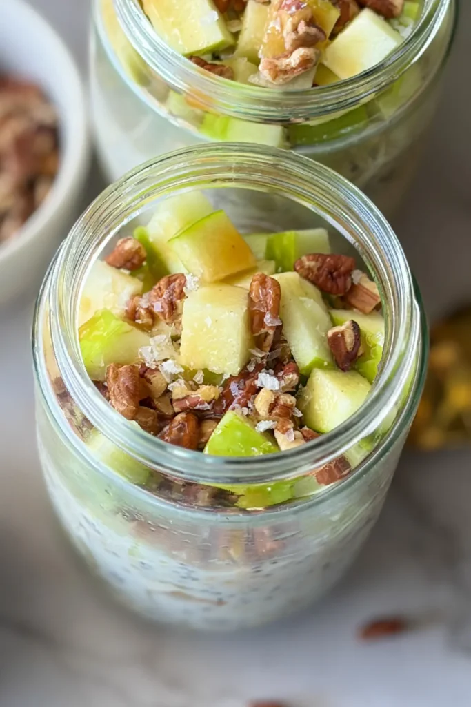A close-up birds-eye view of the top of an open overnight oats jar with diced apples, salt and caramel.