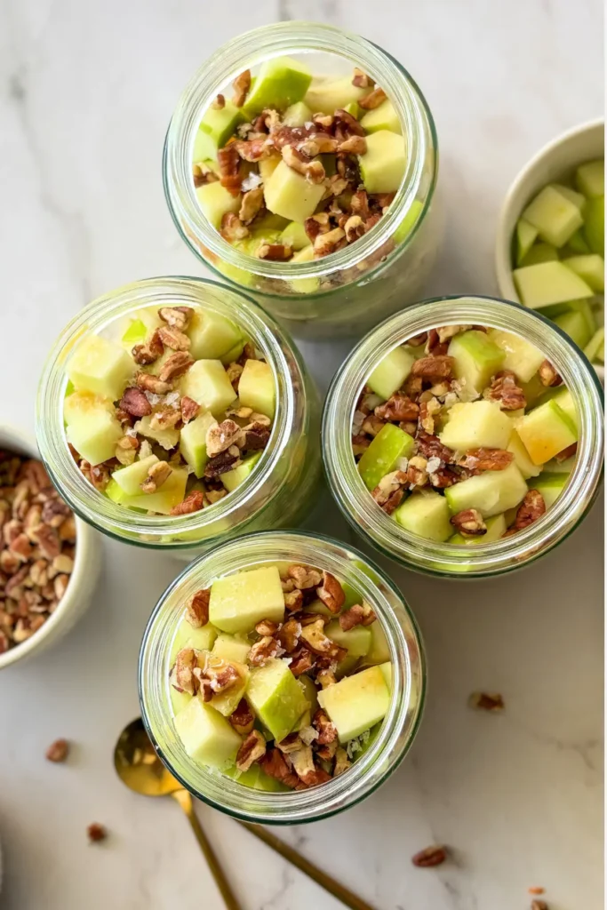 A birds-eye view of four jars of salty caramel apple overnight oats, fully assembled, on a counter in the shape of a diamond.