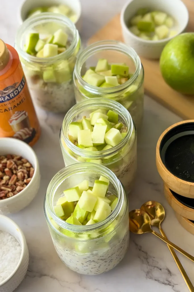 Jars of overnight oats topped with diced Granny smith apples on a counter.