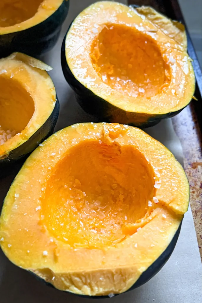 Raw squash halves with oil and salt on a baking sheet.