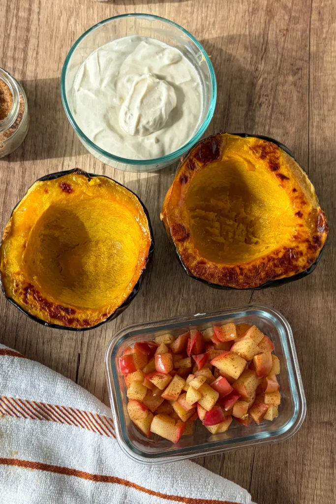 Two squash halves next to a bowl of filling and a bowl of cooked apples for meal prep storage.