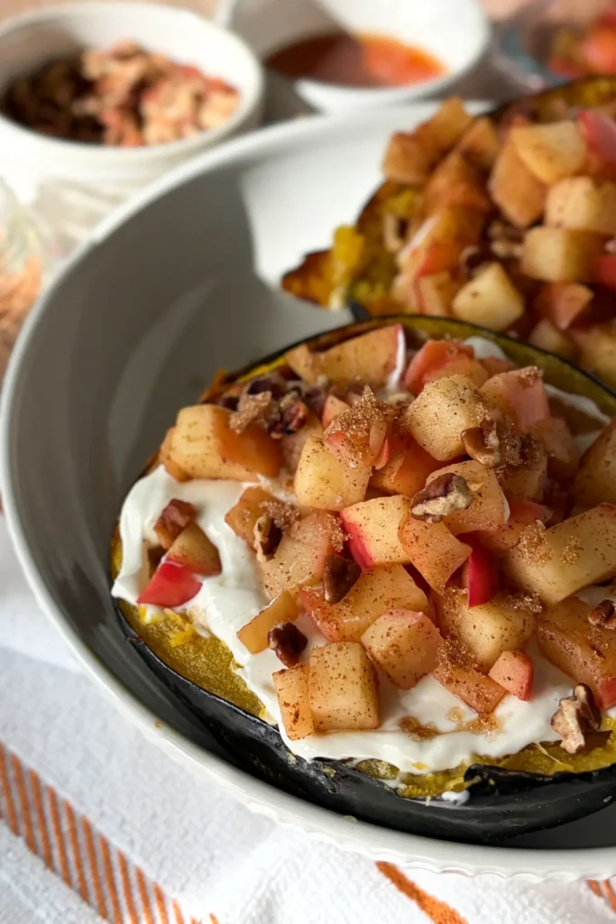 A close-up of two acorn squash boats stuffed with cheesecake filling and apples on a white plate on a fall towel.
