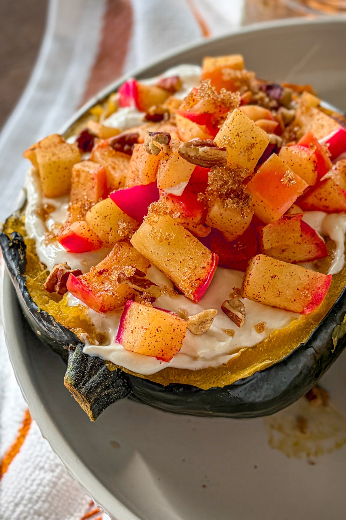 An acorn squash halved and topped with vanilla cheesecake filling, warm cinnamon apples. amd pecans on a white plate.