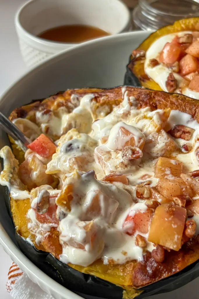 A close-up of a spoon digging into a squash showing the creamy filling in the center mixed with the apples.