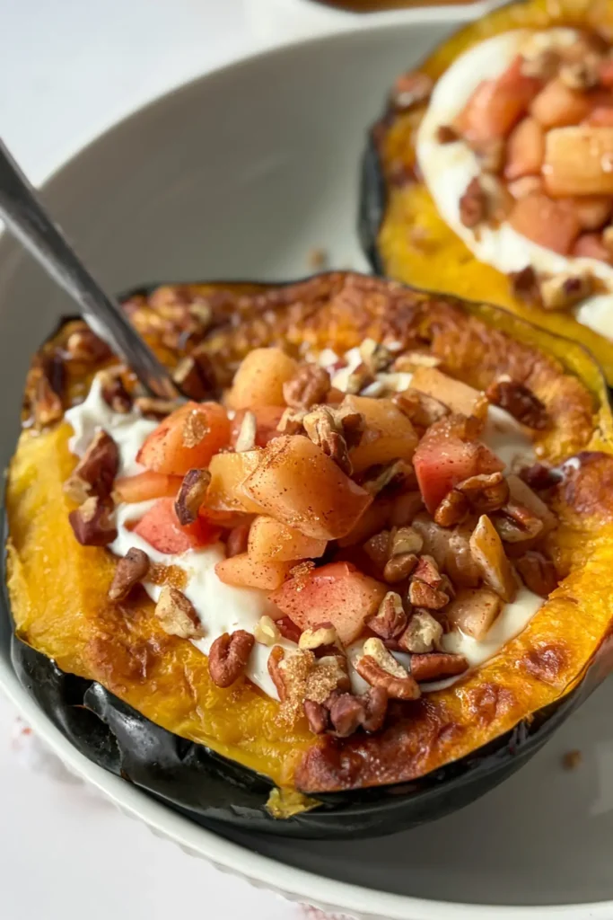 A close-up of the creamy filling with the cinnamon apples in the roasted acorn squash with a spoon it in on a white plate.