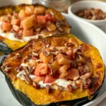 Two fully assembled acorn squash boats, one front and center with a large spoon in it on a white plate.