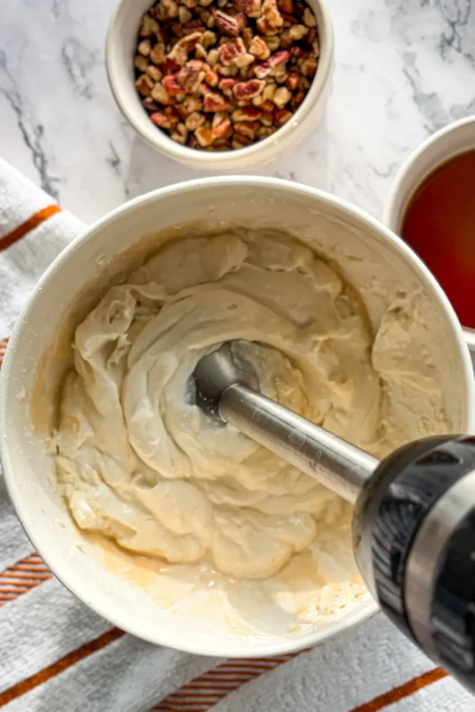 Smooth, creamy cheesecake filling in a bowl being mixed by an immersion blender.